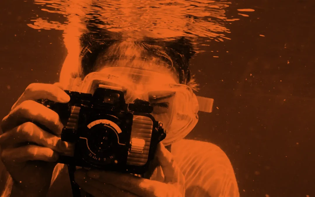 A person under water taking photos, with bubbles rising to the surface
